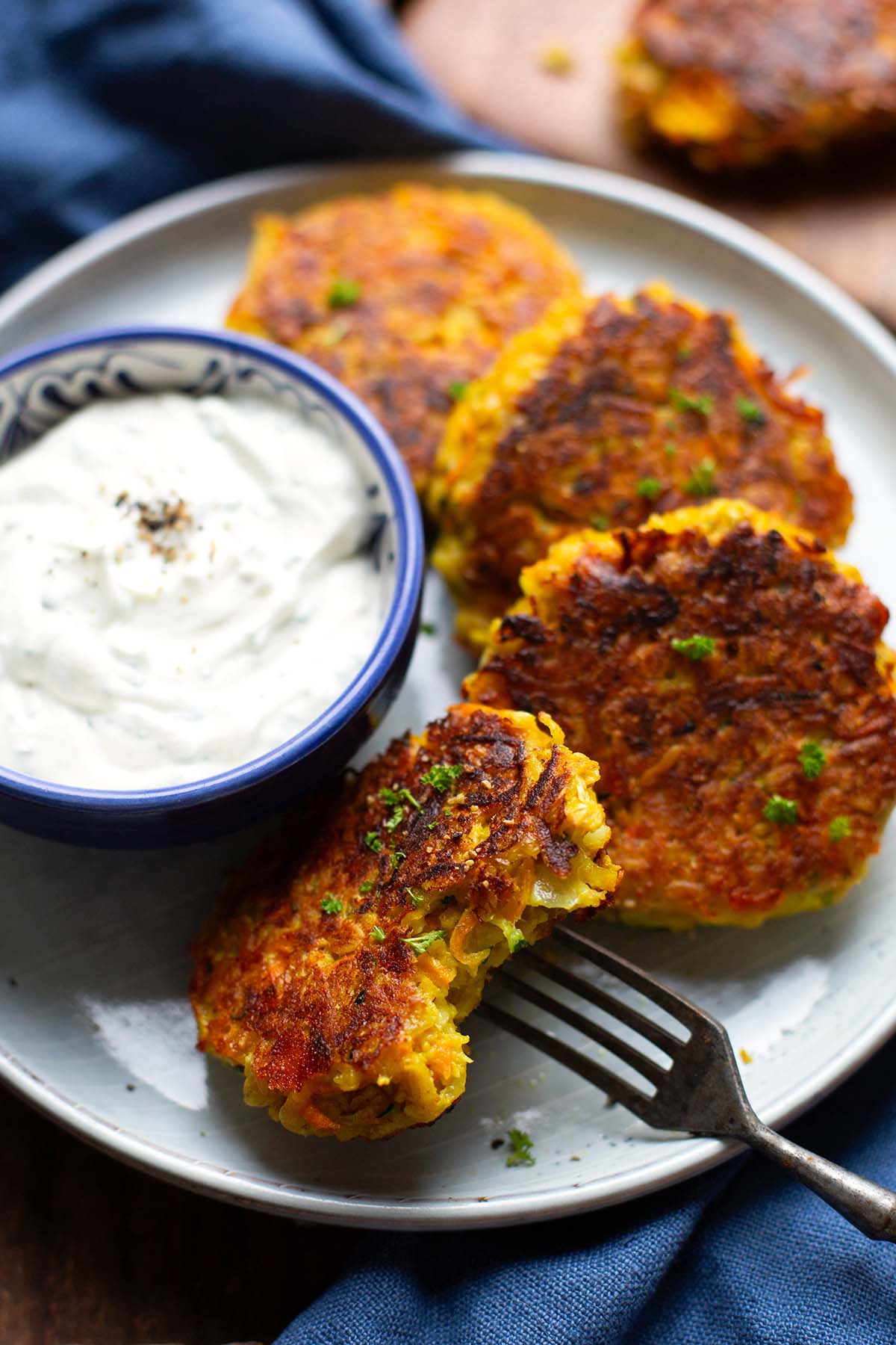 Add finished vegetable frequency on a white plate with a small bowl of herb curd. One of the meatballs is piled up and bitten with a fork.