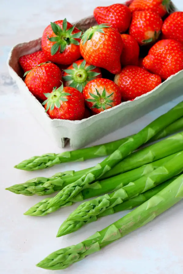 Green asparagus rods and a bowl of strawberries