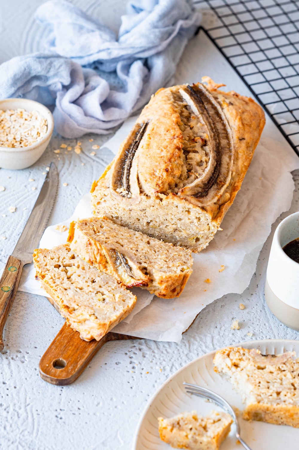 Banana bread without egg served on a board with white butter bread paper. Two pieces have already been cut off and a third is next to it on a plate.