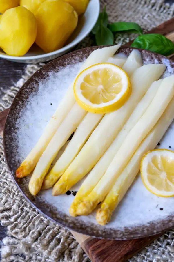 Asparagus cooked in the oven on a plate with a lemon slice.