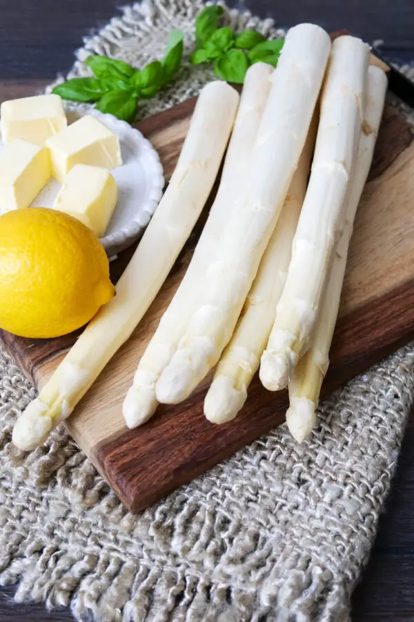 The ingredients to cook asparagus in the oven on a wooden board.