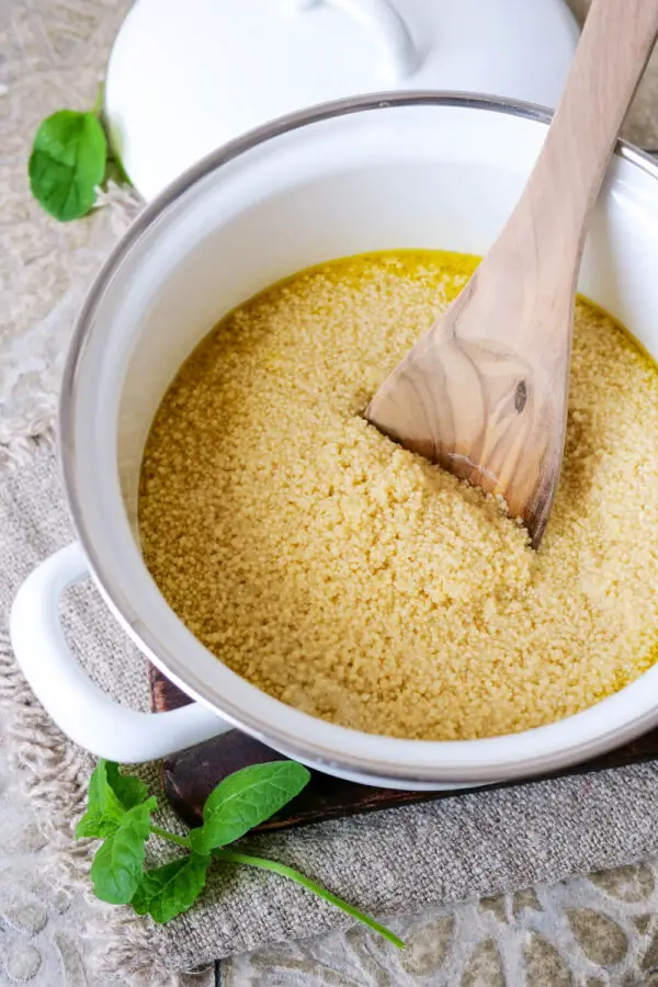 Couscous in a saucepan with a wooden spoon that is currently being prepared.