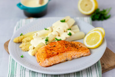 Asparagus with salmon, sauce and lemon slices arranged on a plate.