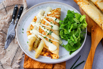 Asparagus with pancakes, sauce and salad arranged on a plate.