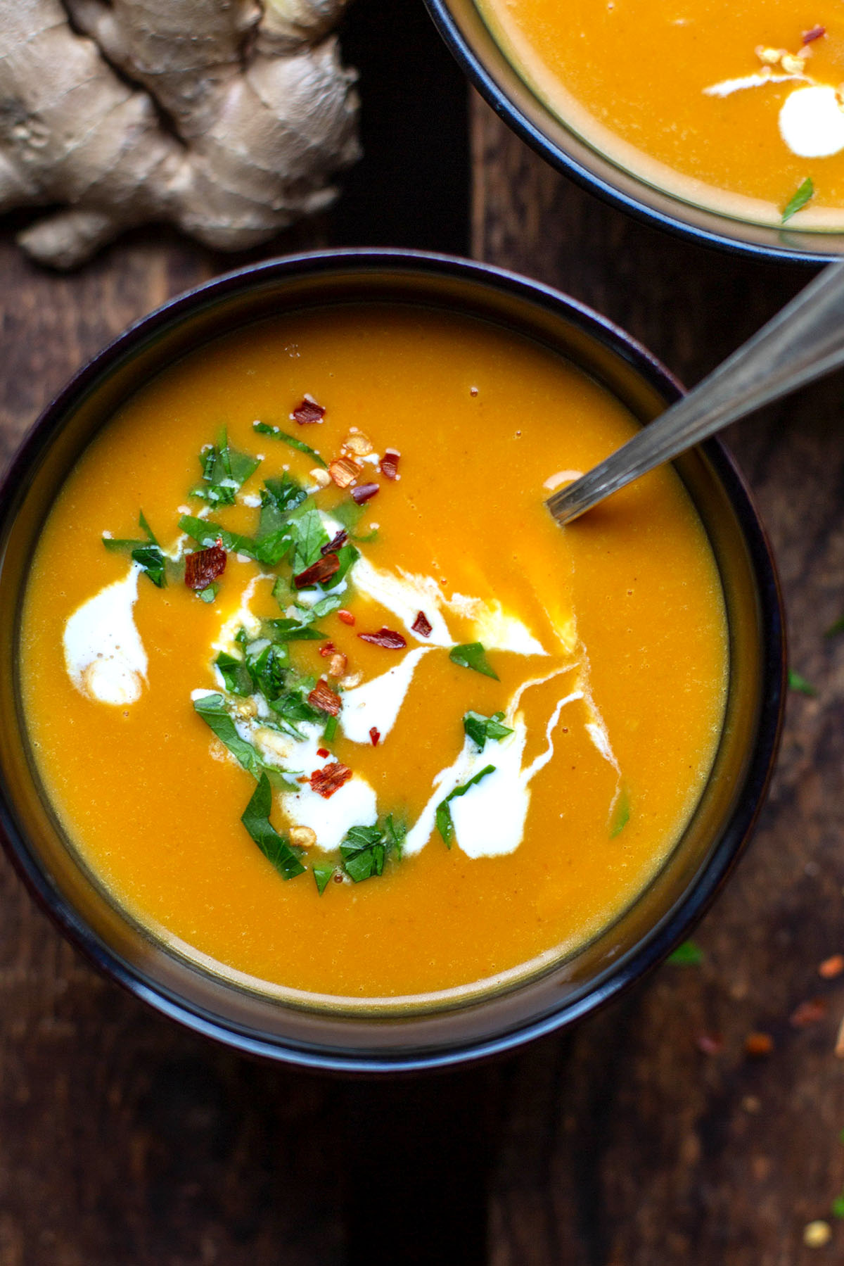 Sweet potato soup with coconut milk and ginger in a black bowl. Topped with chilli flakes and parsley