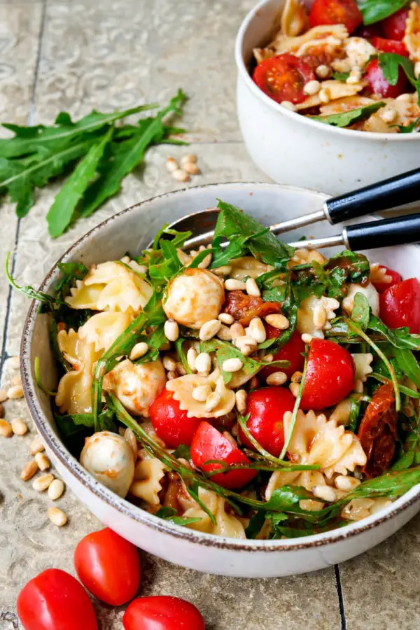 Italian pasta salad with arugula, mozzarella, tomatoes and pine nuts in the gray bowl