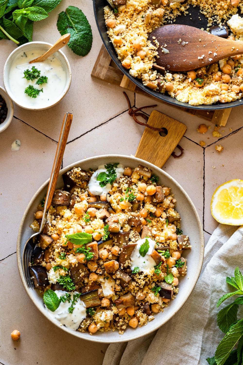 Auberginen couscous with chickpeas and feta Auberginen couscous with chickpeas and feta served in a bowl, next to it the pan and a yogurt mint dip.