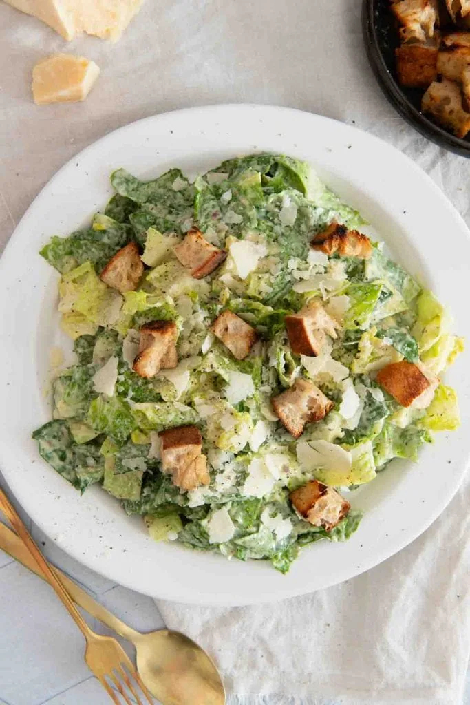 A plate with a classic original Caesar Salad: Roman salad in a creamy dressing, garnished with large croutons, planed parmesan and black pepper
