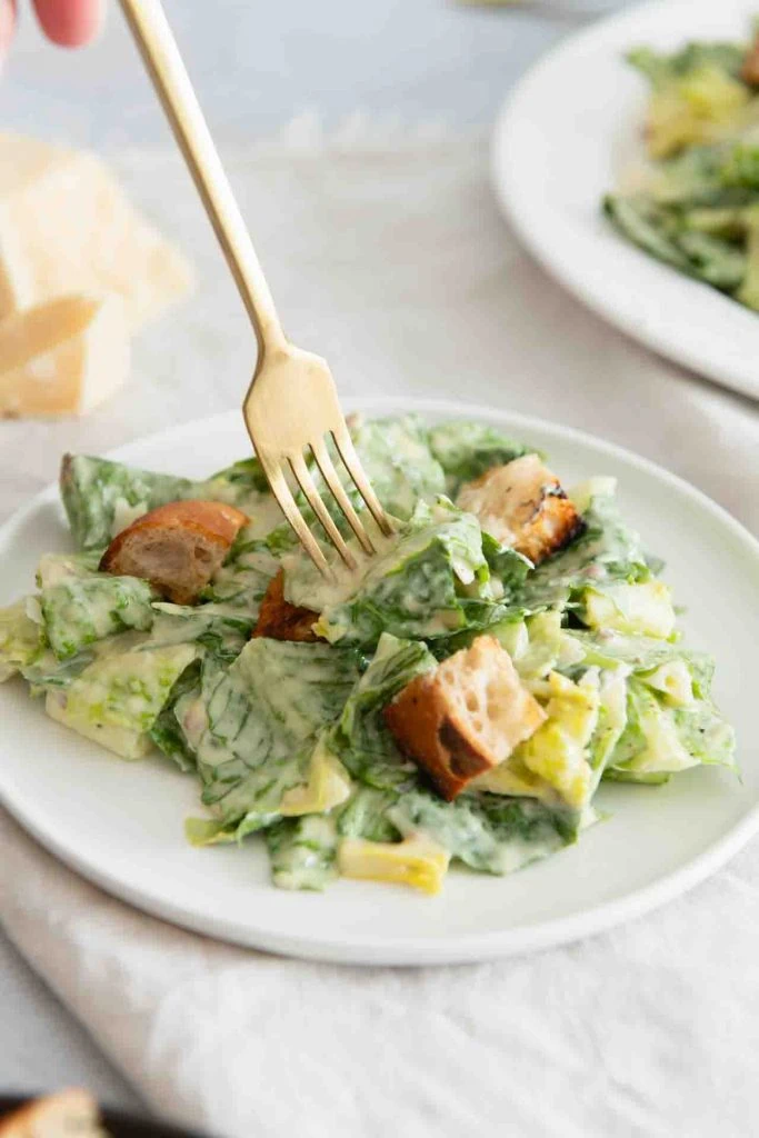 A plate with Caesar Salad (Roman salad, croutons, parmesan, dressing), a golden fork sticks into the salad.