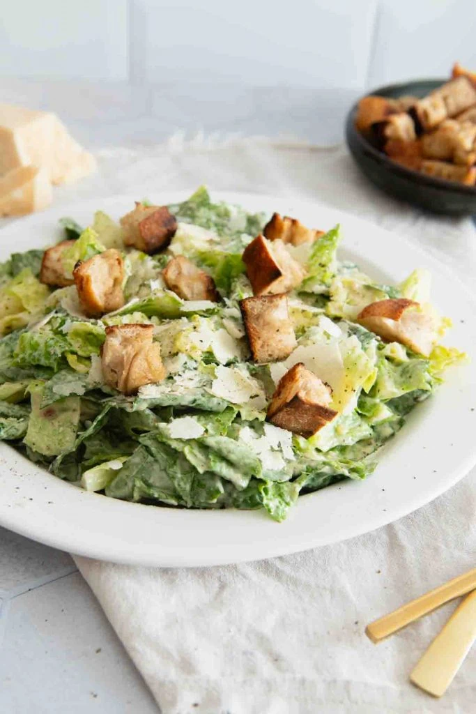 A plate with a classic Caesar Salad: Roman salad in a creamy dressing, garnished with large croutons, planed parmesan and black pepper